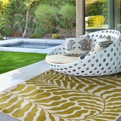 Poltrona oval branca com padrão recortado e almofadas decorativas junto a tapete com padrão de folhas, piscina e jardim.