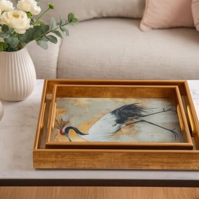 Três tabuleiros de madeira com desenho de garça, vaso branco com flores e pera decorativa numa mesa de mármore.