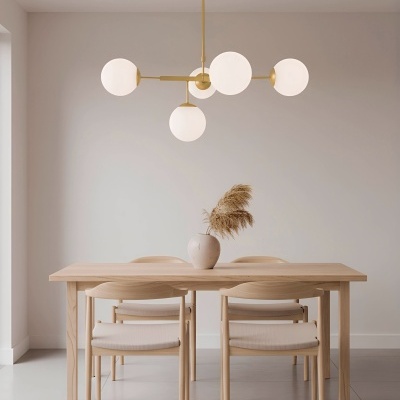 Mesa de madeira clara com quatro cadeiras e candeeiro suspenso com globos brancos numa sala de jantar minimalista.