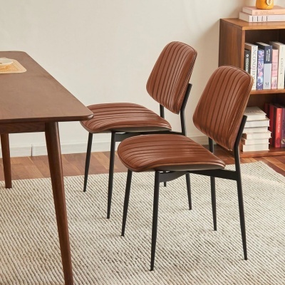 Duas cadeiras castanhas estofadas com estrutura preta numa sala com tapete claro e estante com livros