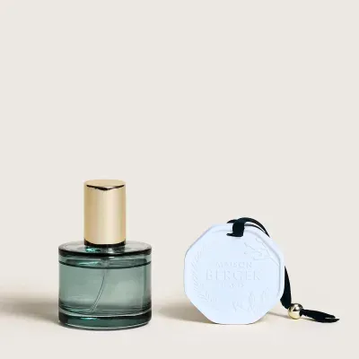 Frasco de vidro verde com tampa dourada e objeto decorativo branco octogonal com cordão preto