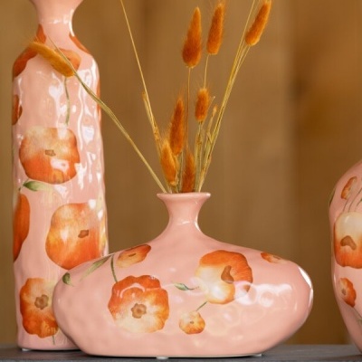 Vasos decorativos cor rosa com flores pintadas laranja e folhas verdes, sobre mesa cinza e fundo de madeira.