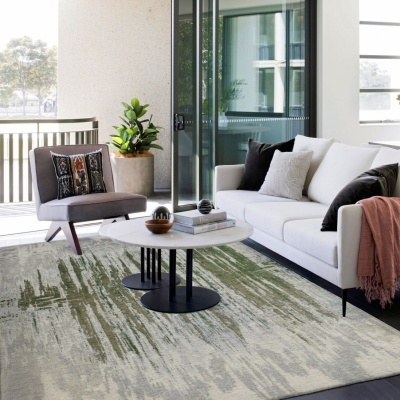 Sala de estar com sofá branco, poltrona cinzenta, mesa de centro redonda e tapete verde e bege.