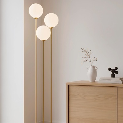 Candeeiro de pé dourado com globos brancos ao lado de cómoda de madeira clara com jarra branca e livros