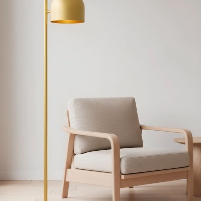 Lâmpada de pé dourada minimalista ao lado de poltrona de madeira clara com almofadas cinza