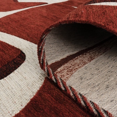 Tapete vermelho e creme com padrão geométrico e bordas enroladas mostrando o avesso listrado.