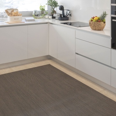 Cozinha moderna com móveis brancos, bancada branca, máquina de café preta, fruteira de palha e tapete cinza escuro no chão.