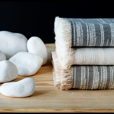 Três tapetes listrados com franjas ao lado de pedras brancas sobre madeira