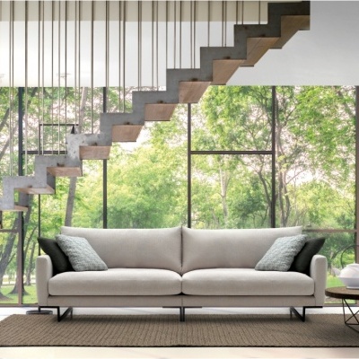 Sofá cinzento claro com almofadas verdes e mesa de centro numa sala moderna com escadas e grandes janelas