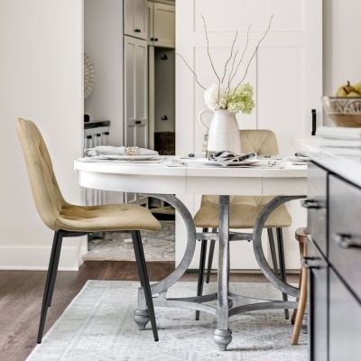 Mesa de jantar branca redonda com cadeiras estofadas bege e jarra decorativa