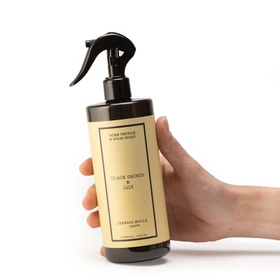 frasco preto de spray para ambiente com etiqueta amarela e texto em inglês segurado por uma mão