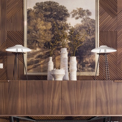 Aparador de madeira com vasos de cerâmica branca, lâmpadas de tripé e quadro de paisagem na parede de madeira texturizada