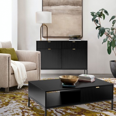 Sala de estar com móveis pretos estriados e detalhes dourados, poltrona bege e planta em vaso cinzento