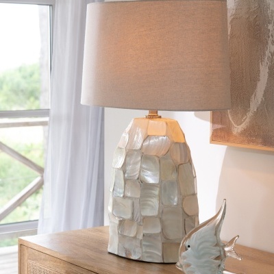 Candeeiro de mesa com base em azulejos iridescentes e abajur cinzento claro em móvel de madeira com escultura de peixe de vidro