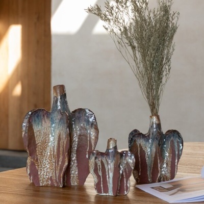Três vasos decorativos de cerâmica em mesa de madeira com ramos secos num deles e livro aberto ao lado.