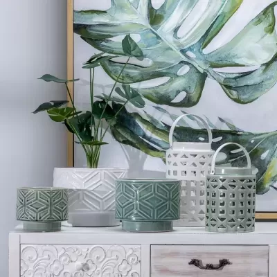 Vasos e lanternas decorativas em cerâmica verde e branca com padrões geométricos em móvel branco