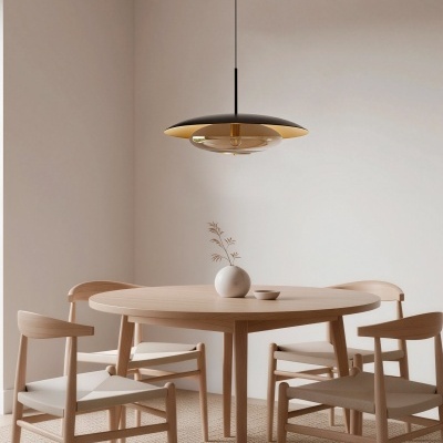 Mesa redonda de madeira clara com quatro cadeiras, vaso branco, prato pequeno, candeeiro pendente preto e dourado