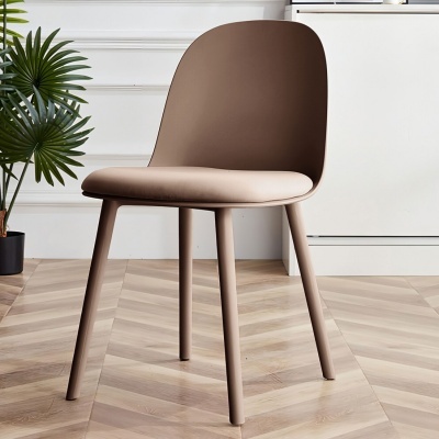 Cadeira castanha estofada com pernas finas em chão de madeira e planta verde ao lado.