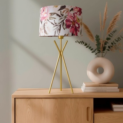 Candeeiro de mesa dourado com cúpula floral sobre móvel de madeira clara com vaso decorativo e livros
