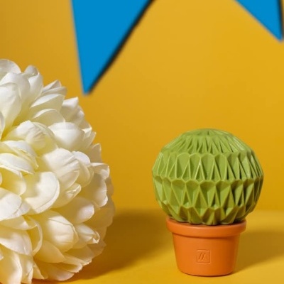 Vaso pequeno de cerâmica com planta decorativa verde feita de papel dobrado em fundo amarelo com decoração azul e flor branca.