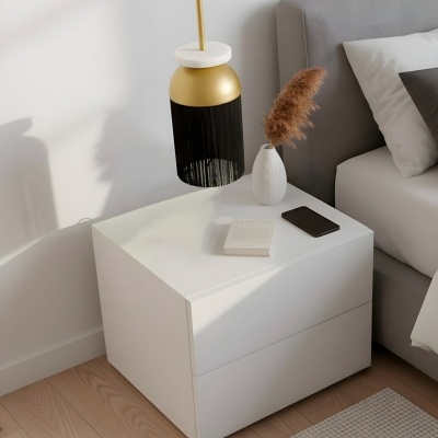 Mesa de cabeceira branca minimalista com abajur dourado e preto e vaso branco com planta ao lado de cama cinzenta