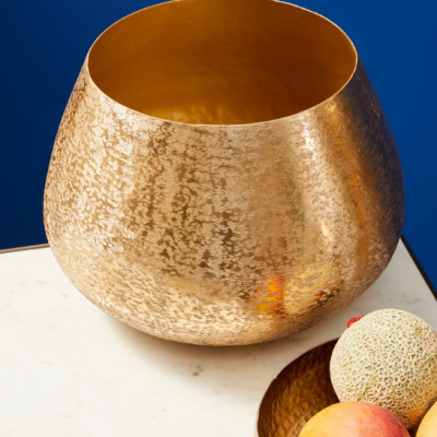 Vasos metálicos dourados martelados com frutas em fruteira sobre mesa de mármore