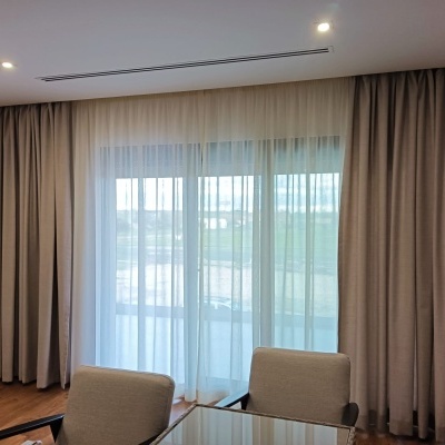 Janela com cortinados bege e cortinas brancas transparentes num interior com cadeiras