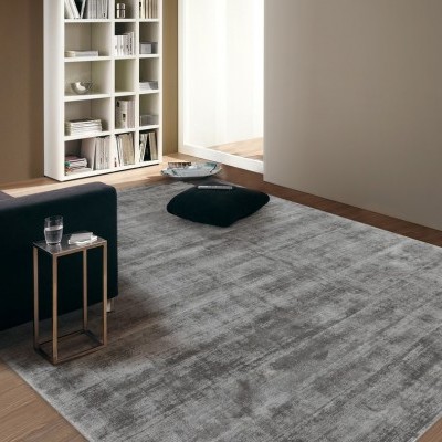 Tapete cinza grande com textura aveludada num quarto minimalista com sofá escuro e estante branca.