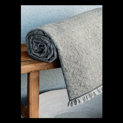 Manta cinzenta padrão geométrico com franjas sobre madeira