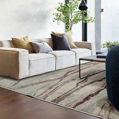 Sofá bege com almofadas coloridas ao lado de mesa de centro e planta, com tapete padrão abstrato no chão