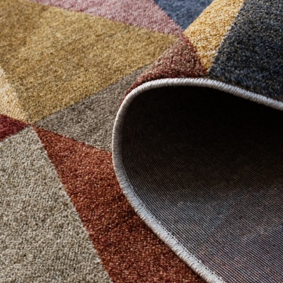 Tapete colorido com padrão geométrico e textura felpuda, parte enrolada a mostrar o verso.