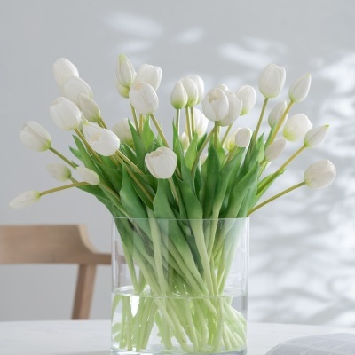 Vaso com tulipas brancas numa mesa com livros e cadeira ao fundo