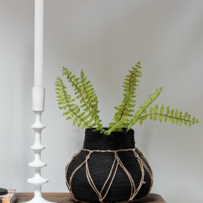 Vaso preto com planta verde ao lado de castiçal branco com vela acesa numa mesa de madeira
