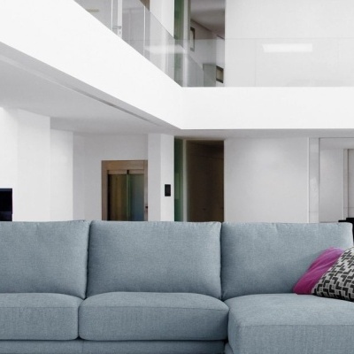 Sofá cinza claro com almofadas decorativas numa sala moderna com escadas de vidro e madeira.