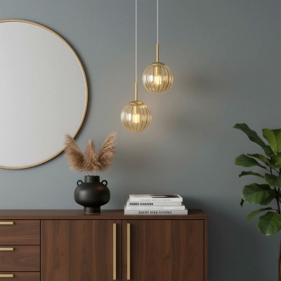 Cómoda de madeira escura com puxadores dourados, espelho redondo dourado, duas luminárias pendentes douradas e planta verde em vaso preto