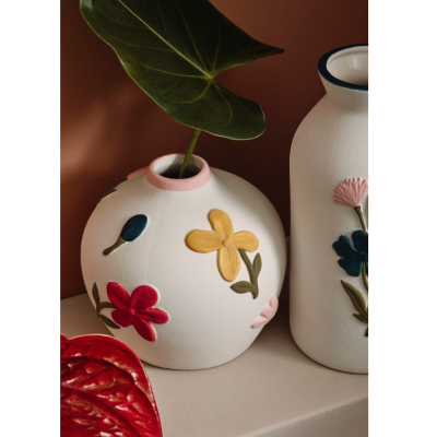 Vasos de cerâmica branca com flores coloridas em relevo sobre superfície clara e parede castanha