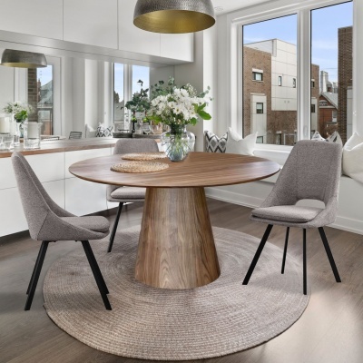 Mesa de jantar redonda em madeira com cadeiras cinzentas numa sala iluminada