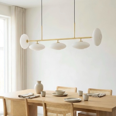 Mesa de jantar em madeira clara com quatro cadeiras de rattan, loiça bege e candeeiro suspenso dourado com cúpulas brancas