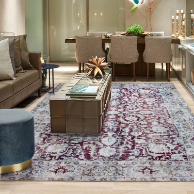 Sala de estar com tapete floral, sofá cinzento e mesa de centro em vidro.