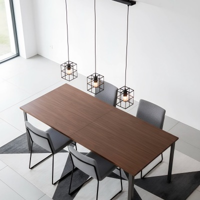 Mesa de madeira com quatro cadeiras cinza e três candeeiros de estrutura metálica preta em forma de cubo suspensos