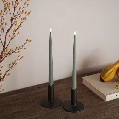 Dois castiçais pretos com velas verdes acesas sobre mesa de madeira com decoração