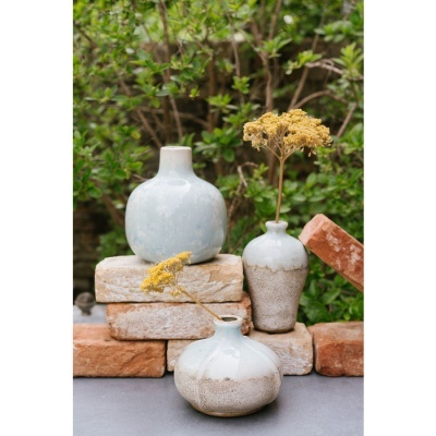 Conjunto de três vasos de cerâmica com flores secas sobre tijolos com folhagem ao fundo