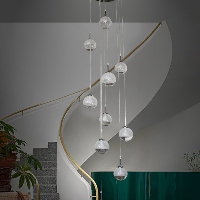 Candeeiro pendente com esferas de vidro transparente suspensas em cabos finos em ambiente com escada curva cinza