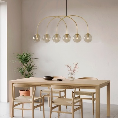 Mesa de madeira clara com quatro cadeiras bege, candeeiro com globos de vidro e planta em vaso terracota.