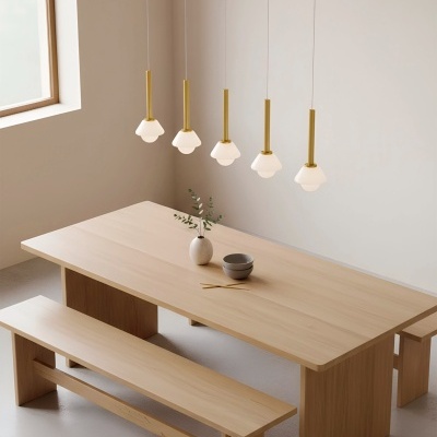 Mesa de jantar de madeira clara com bancos e luminária pendente com cinco candeeiros brancos em forma de flor
