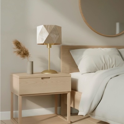 Mesa de cabeceira de madeira clara com candeeiro dourado e vaso com plantas secas ao lado de cama com roupa branca