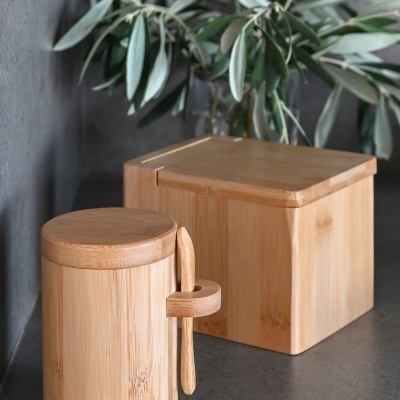 Recipientes de madeira clara com tampa e colher, ramo de folhas verdes ao fundo