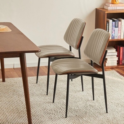 Duas cadeiras bege riscado com pernas pretas ao lado de mesa de madeira numa sala com estante