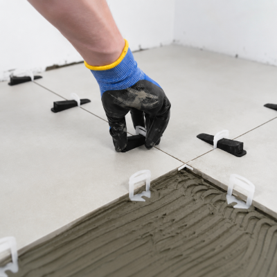 Mão com luva a instalar azulejos cerâmicos cinza claro com espaçadores de plástico sobre argamassa