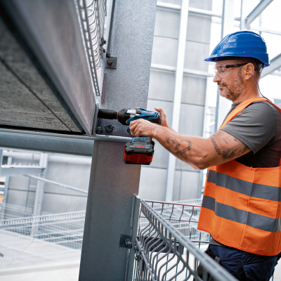 Homem a usar ferramenta elétrica numa estrutura metálica num ambiente industrial